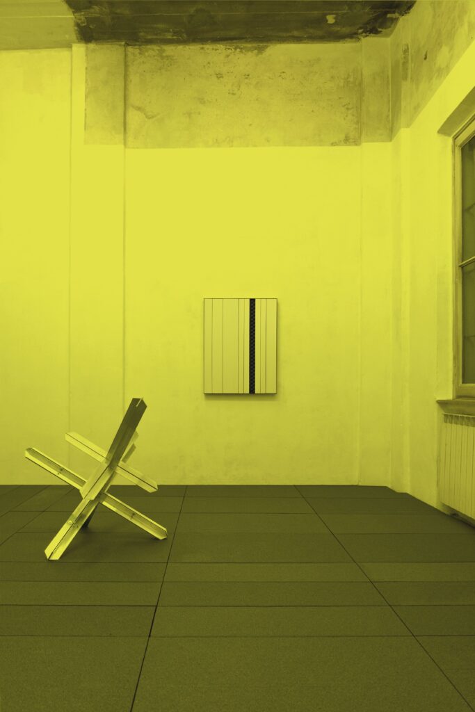 Installation view of *24:00>00:01*: an XPS panel and an aluminum sculpture on a floor decorated with gray polystyrene, in a space illuminated by yellow light